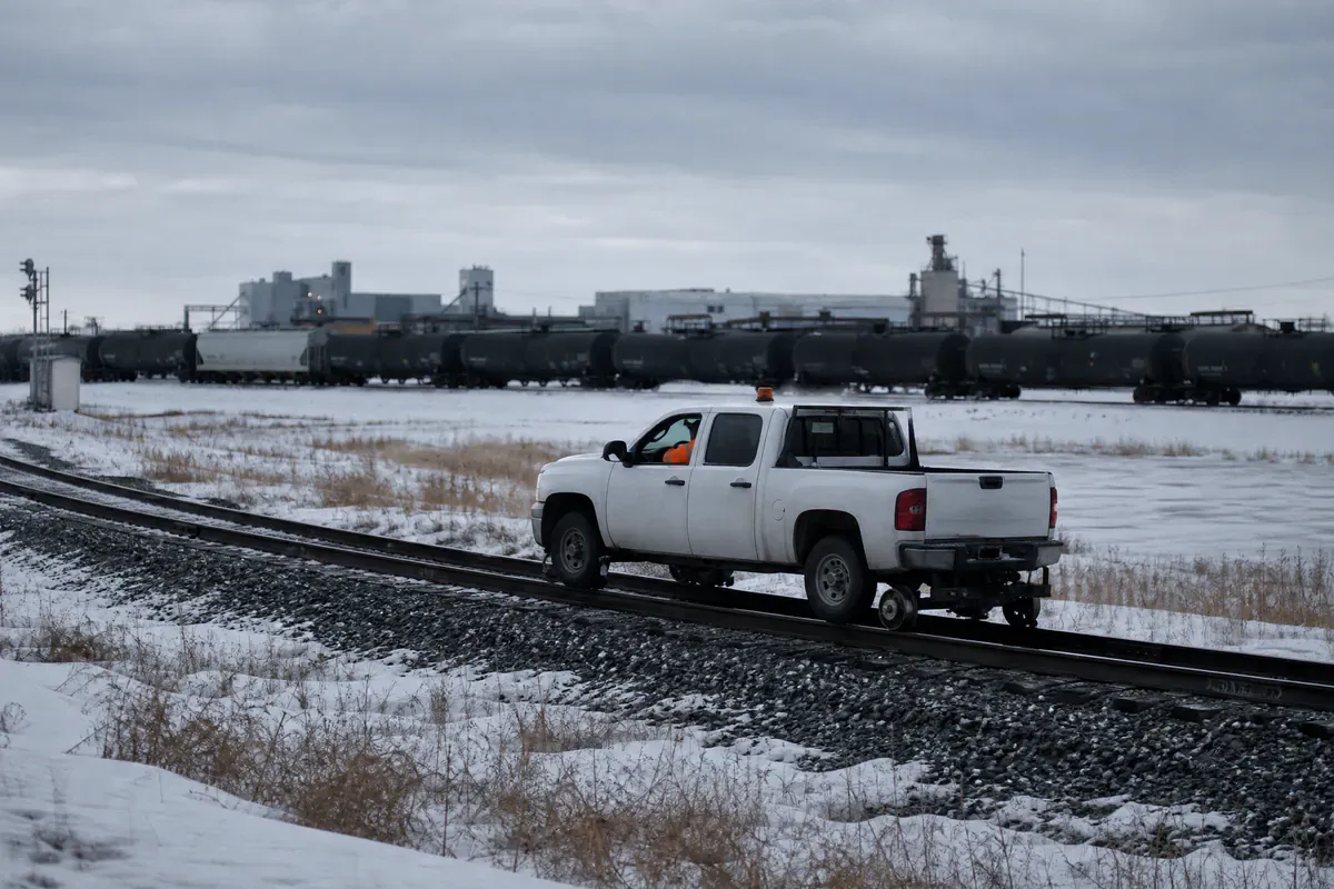 Hi-rail pickup with guide wheels on the rails travelling a snowy spur past a row of tank cars