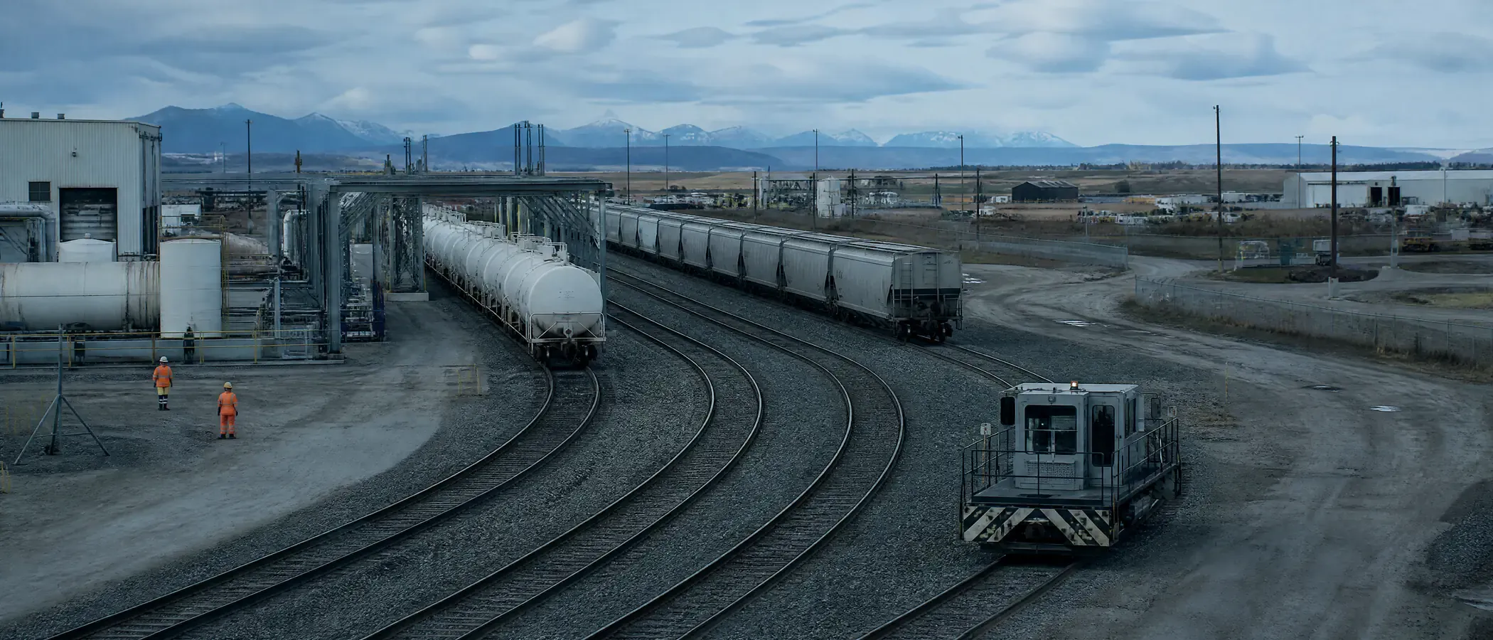 Alberta plant rail yard with tank cars at a loading rack, covered hoppers and foothills beyond